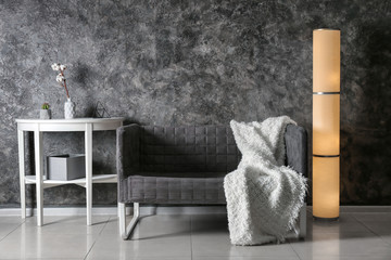 Modern interior of living room with stylish sofa, table and lamp near dark wall