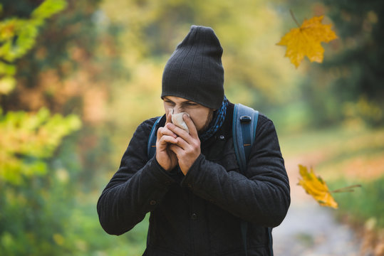 man sneezes and blows his nose in a handkerchief in an autumn park