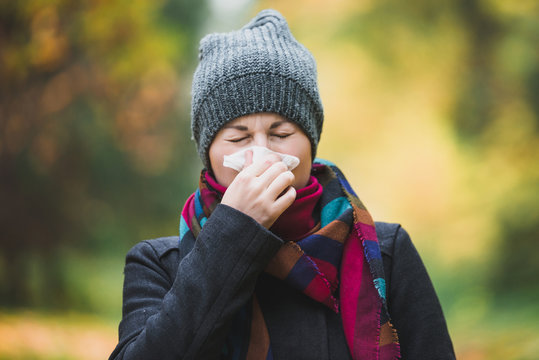 Woman sneezes and blows his nose in a handkerchief in an autumn park