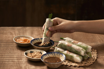 Young woman's hands eating healthy spring roll dipped in a soya sauce. Selective focus.