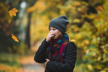 Woman sneezes and blows his nose in a handkerchief in an autumn park