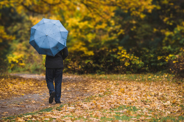 Man under blue umbrella walks in the park in autumn