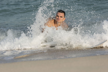 Muscular athletic white caucasian European male on Surfboard body surfing the splashing waves on a beach smiling happily