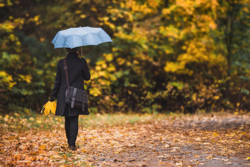 Woman under blue umbrella walks in the park in autumn