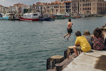 Fototapeta na wymiar Bayonne, France - June 25, 2014 - a group of children watching a boy jump from a pier into the sea