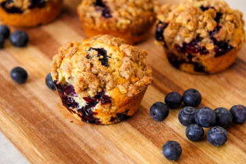 freshly baked blueberry muffins with an oat crumble topping on a natural wooden board