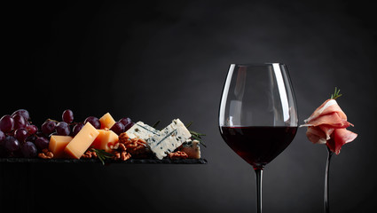 Verre de vin rouge avec divers fromages, fruits et prosciutto.