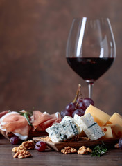 Glass of red wine with various cheeses , fruits and prosciutto .