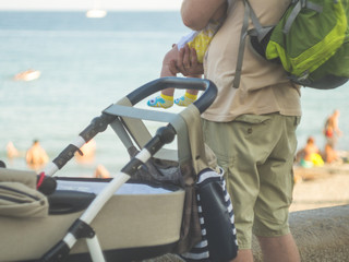 back view of father holding baby kid in arms standing near the storoller walking outdoors family concept