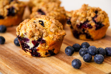 freshly baked blueberry muffins with an oat crumble topping on a natural wooden board
