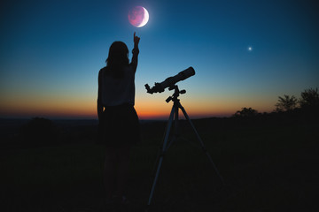 Obraz premium Girl looking at lunar eclipse through a telescope. My astronomy work.