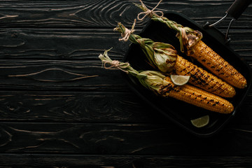 top view of griddle pan with grilled corn and lime slices on wooden table