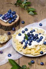 Tasty pasta with fresh organic blueberries and vanilla cream. Sweet dinner on retro wooden table.