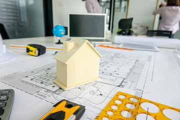 A wooden house model places on architect blueprint plan, laptop and engineering tools background in...