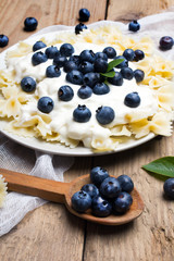 Tasty pasta with fresh organic blueberries and vanilla cream. Sweet dinner on retro wooden table.
