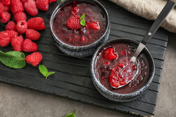 Bowls with sweet raspberry jam and fresh berries on wooden board