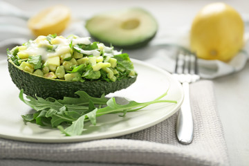Plate with tasty vegetable salad in avocado half on table