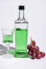 crystal glass and bottle of absinthe with branch of grapes on white
