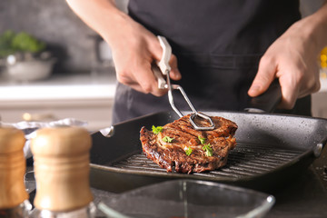 Man with tongs cooking tasty meat in kitchen