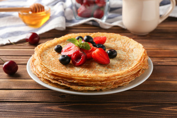 Plate with tasty pancakes and berries on wooden table