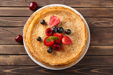 Plate with tasty pancakes and berries on wooden table