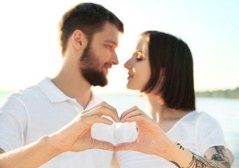 Happy lovely couple making heart with their hands near river on sunny day