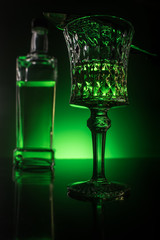 close-up shot of glass with absinthe and bottle on reflective surface and dark green background