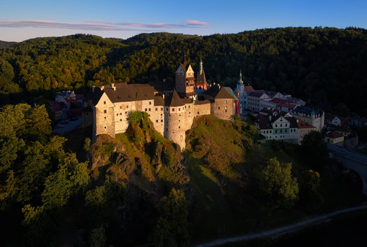 Aerial view on Loket Castle, Burg Elbogen, gothic style castle surrounded by medieval city and green hills, massive fortification illuminated by setting sun. Close to Karlovy vary, Czech republic.