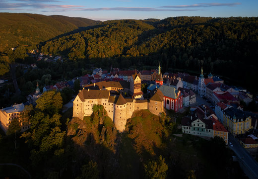 Aerial view on Loket Castle, Burg Elbogen, gothic style castle surrounded by medieval city and green hills, massive fortification illuminated by setting sun. Close to Karlovy vary, Czech republic.