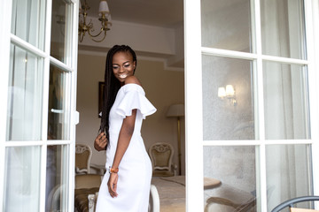 Young afro american woman with african braids or dreadlocks. Girl standing near the open glass door...