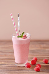 Glass with tasty raspberry smoothie on wooden table against color background