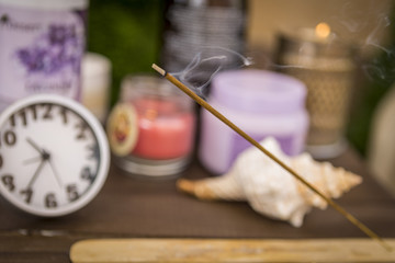 an aromatic Chinese stick that smokes and smoke against a clock and essential oils for massages and spa treatments. accessories for spa massages and a wonderful background.