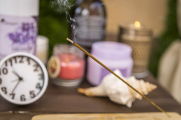 an aromatic Chinese stick that smokes and smoke against a clock and essential oils for massages and spa treatments. accessories for spa massages and a wonderful background.