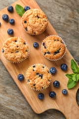 Wooden board with tasty blueberry muffins on table
