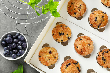 Box with tasty muffins and bowl of fresh blueberries on table