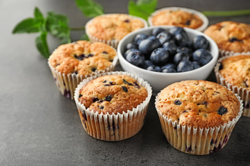 Tasty blueberry muffins and bowl with fresh berries on table, closeup