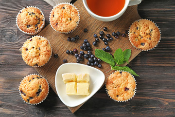 Tasty blueberry muffins with butter and cup of tea on wooden table