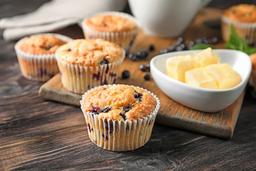 Tasty blueberry muffins with butter on wooden table