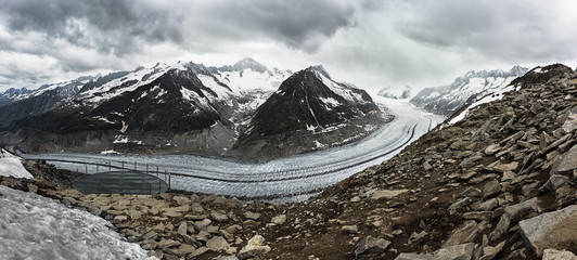 Aerial panoramic view of the Aletsch Glacier in the Swiss Alps with snowy rocky mountains and the dramatic cloudy sky