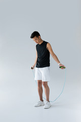 young asian male athlete exercising with jump rope on grey background - obrazy, fototapety, plakaty