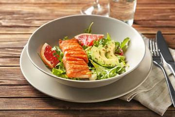 Bowl with fresh salad and fish on wooden table