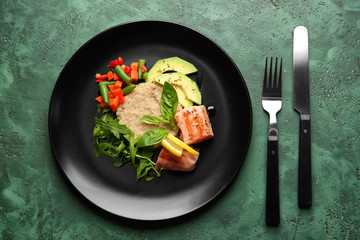Plate with fresh salad and fish on green table