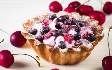 Fresh fruit and berry tart dessert with toss sugar on wooden background. Delicious sweet cake with raspberries, figs, strawberries, cherry, and cream.
