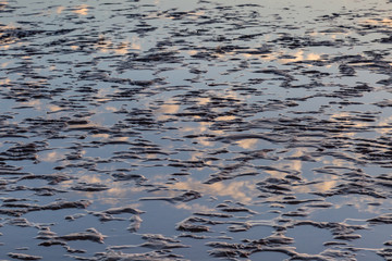 Full frame photograph of pooled water on a sandy beach with reflections of clouds