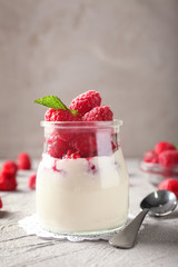 Glass jar with tasty raspberry dessert on table