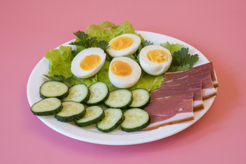 breakfast. Boiled eggs, bacon, greens in a white plate on pink background