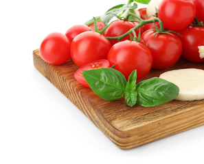 Board with ripe cherry tomatoes, cheese and herbs on white background