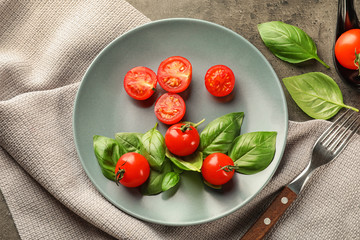 Plate with ripe cherry tomatoes and herbs on grey background