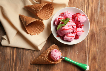 Plate with delicious raspberry ice-cream and waffle cones on wooden table