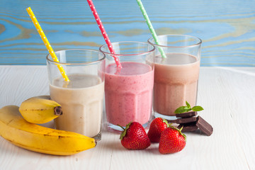 Glasses of milkshakes with chocolate, strawberry, banana flavor, with ice cream on wooden blue and white background. Sweet drinks for summer concept. Shakes and smoothies. Milk shake and cocktail.